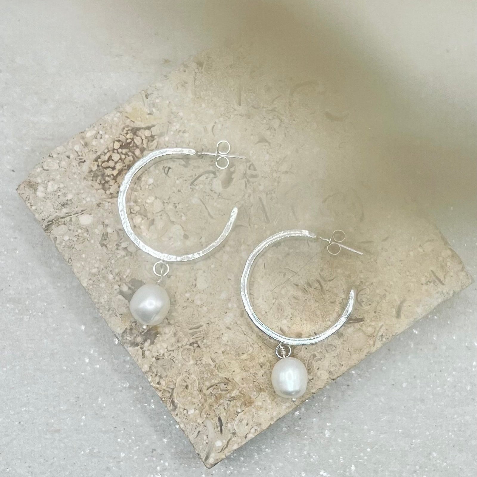 Silver hoop earrings with pearl drops on a stone surface