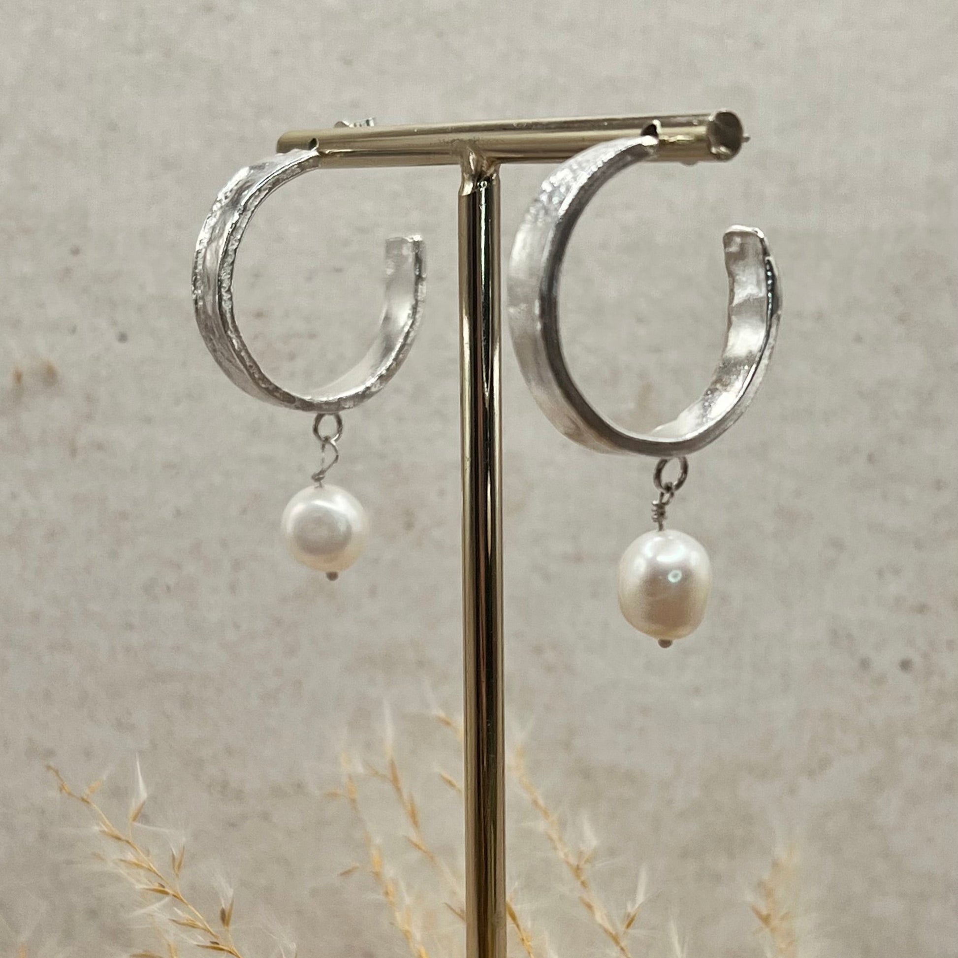 Silver hoop earrings with pearl drops on a stand against a neutral background