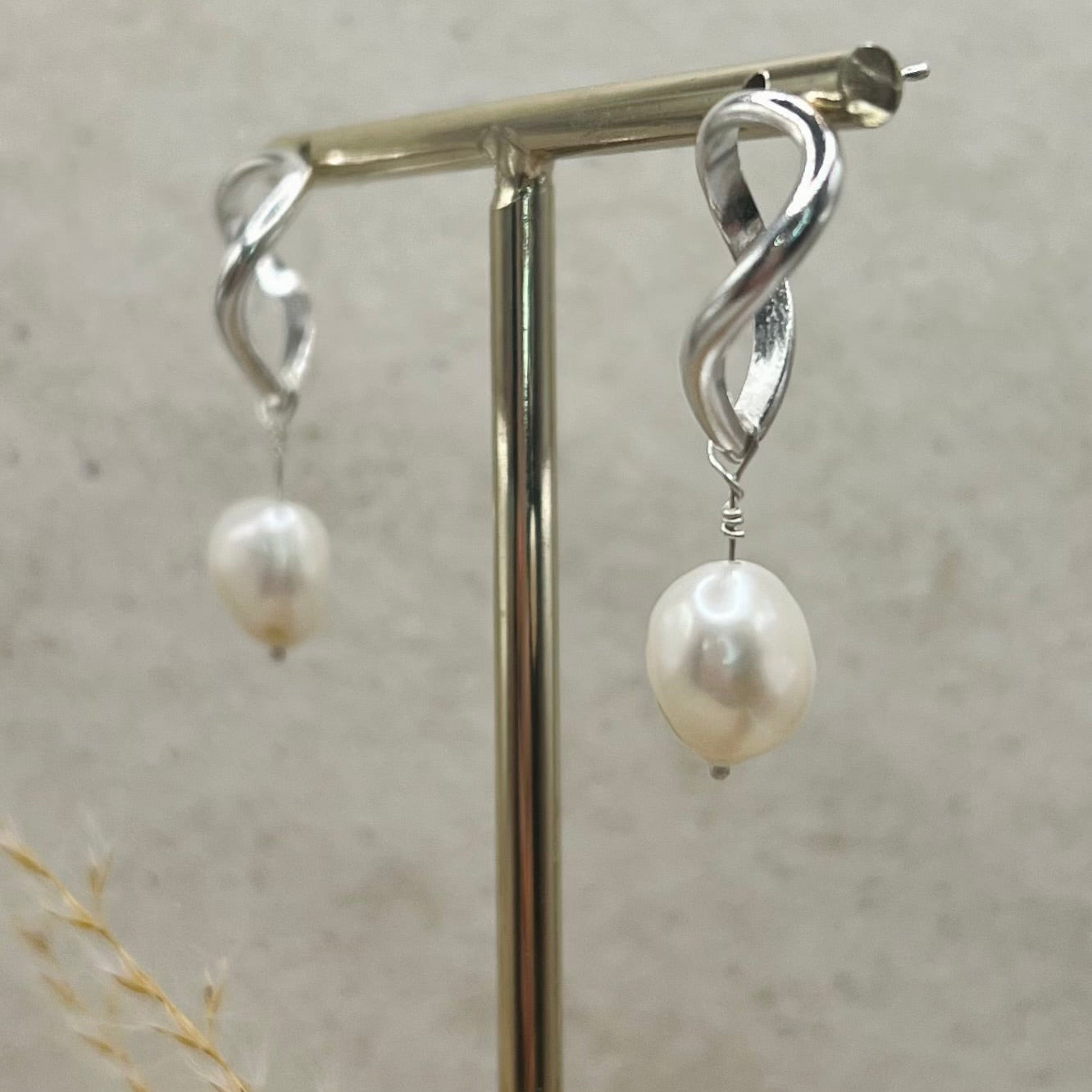 Silver earrings with pearl drops on a stand against a neutral background