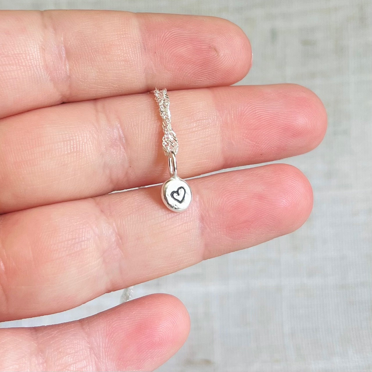 Beautiful little recycled silver nugget necklace held in hand, the little nugget is about one third or the width of a finger.