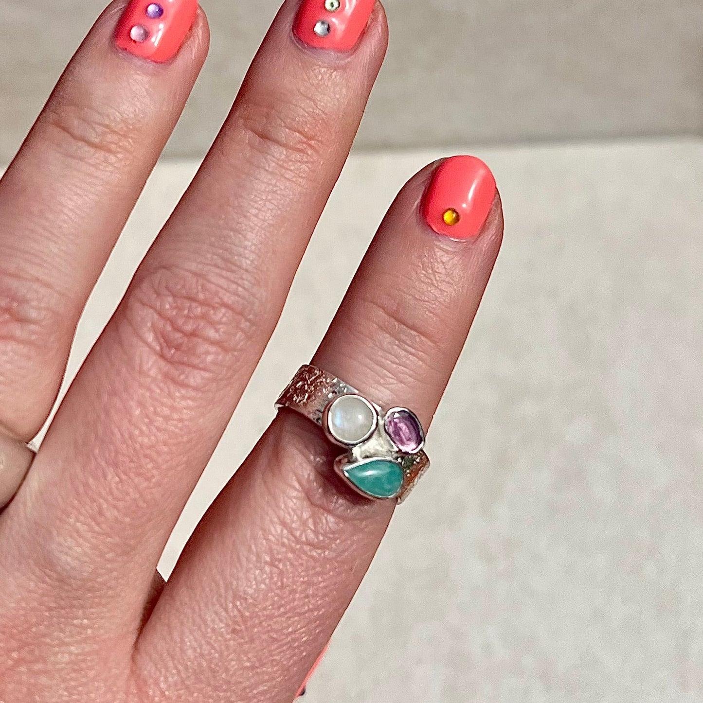 Hand with pink nail polish and a ring featuring a turquoise stone on a neutral background
