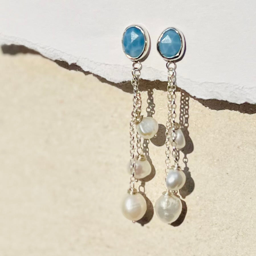 Pair of earrings with blue gemstones and pearl drops on a textured surface