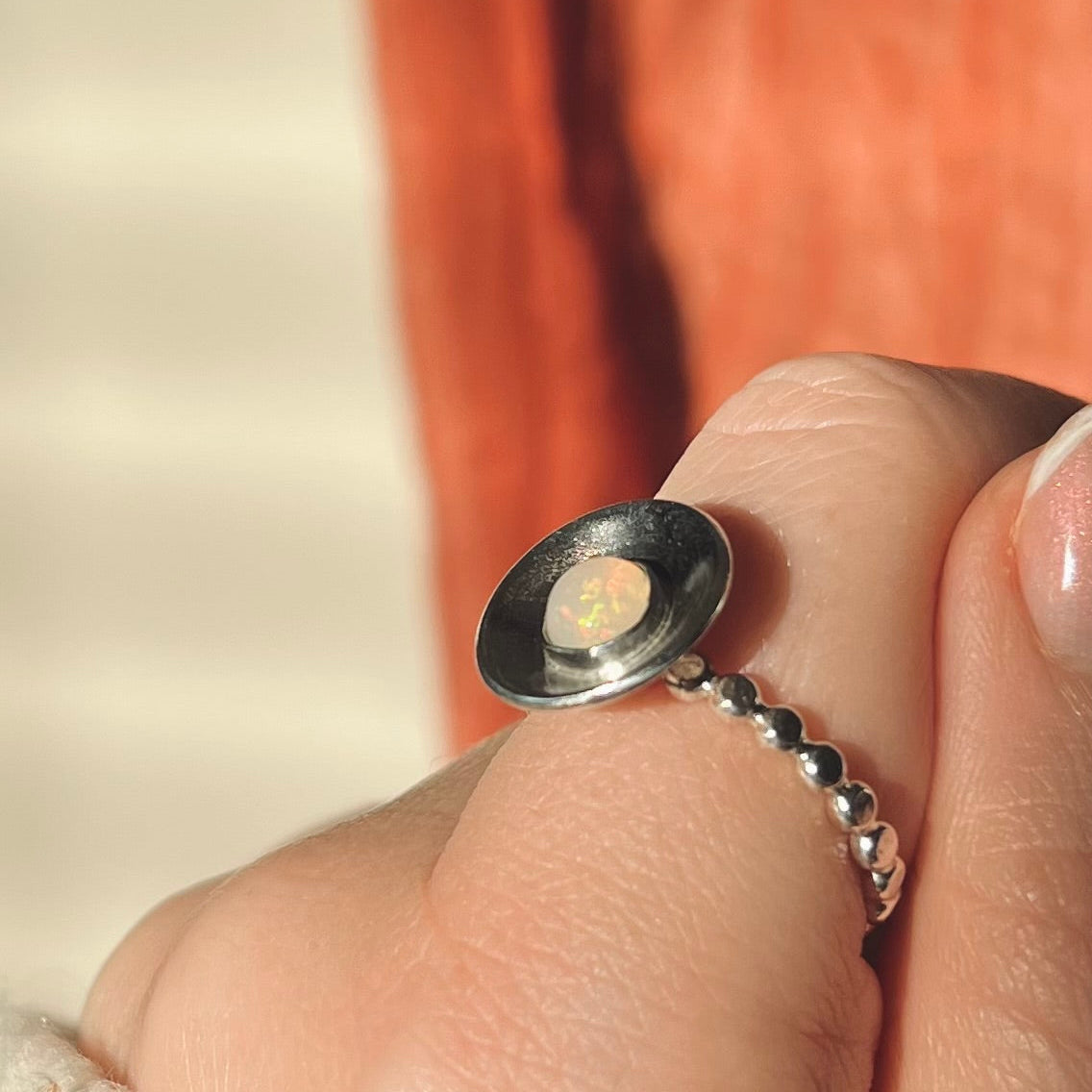 Close-up of a hand wearing a silver ring with an opal stone.