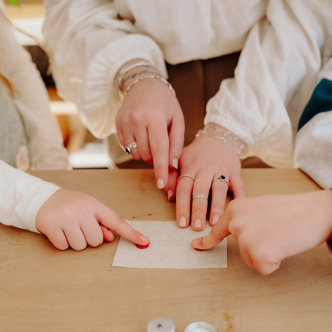 Fingerprint jewellery in the making with fingers being pressed into wax on a wooden table.
