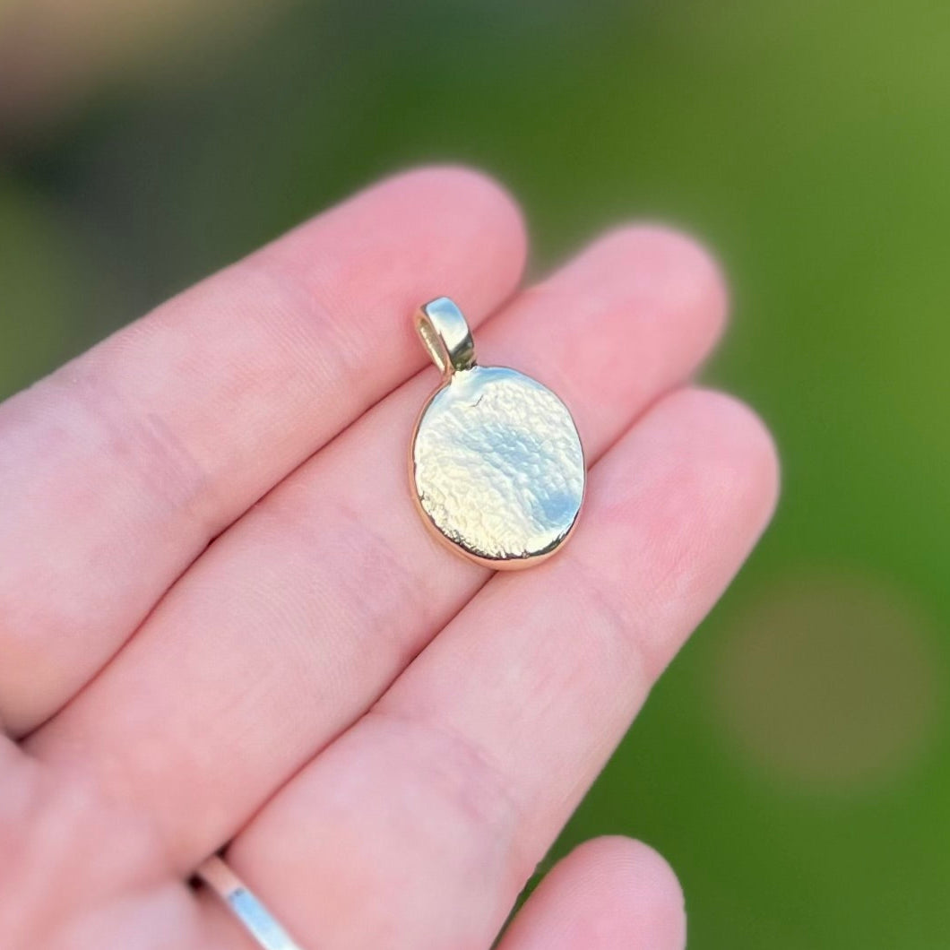 Gold pendant held in a hand with a blurred green background