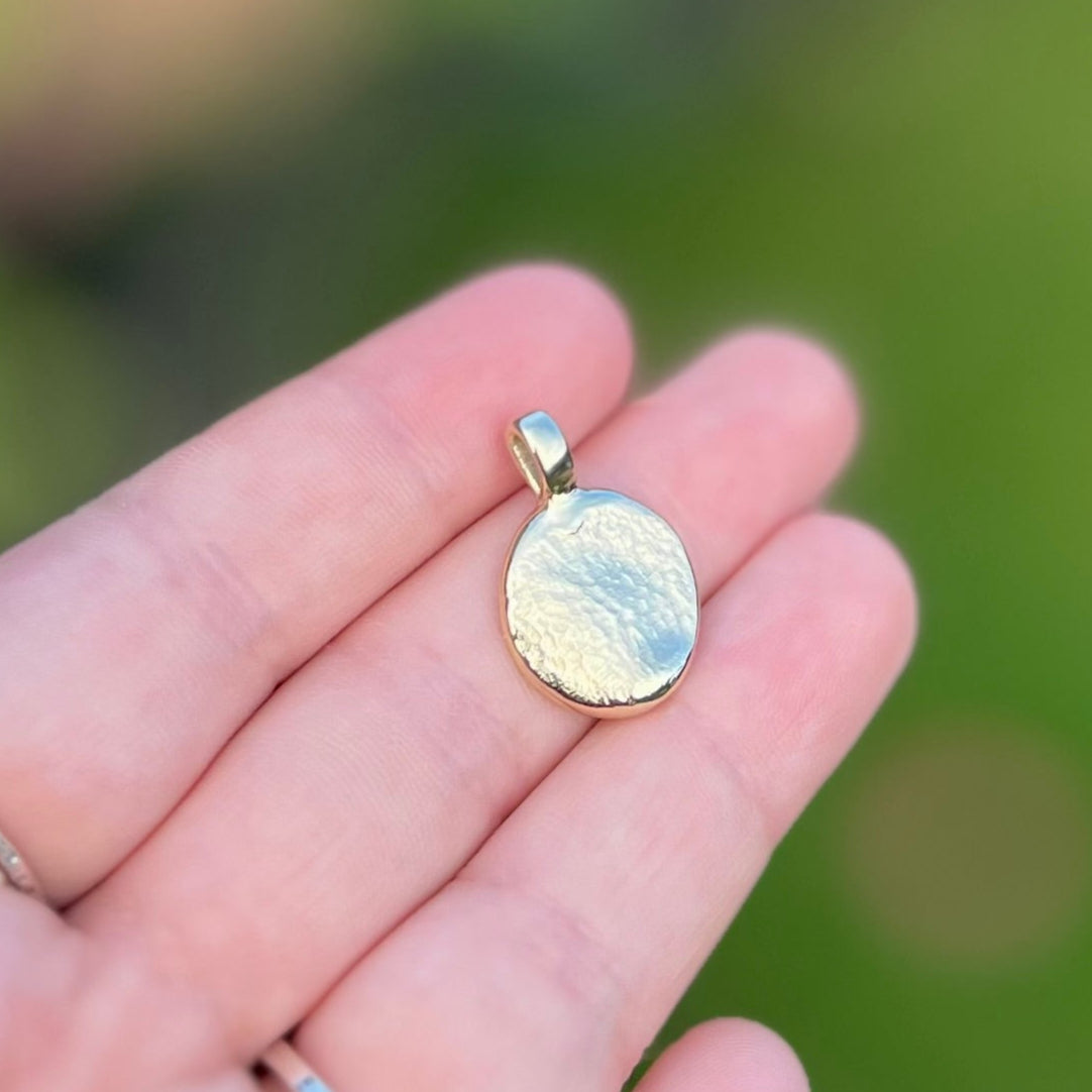 Gold pendant held in a hand with a blurred green background