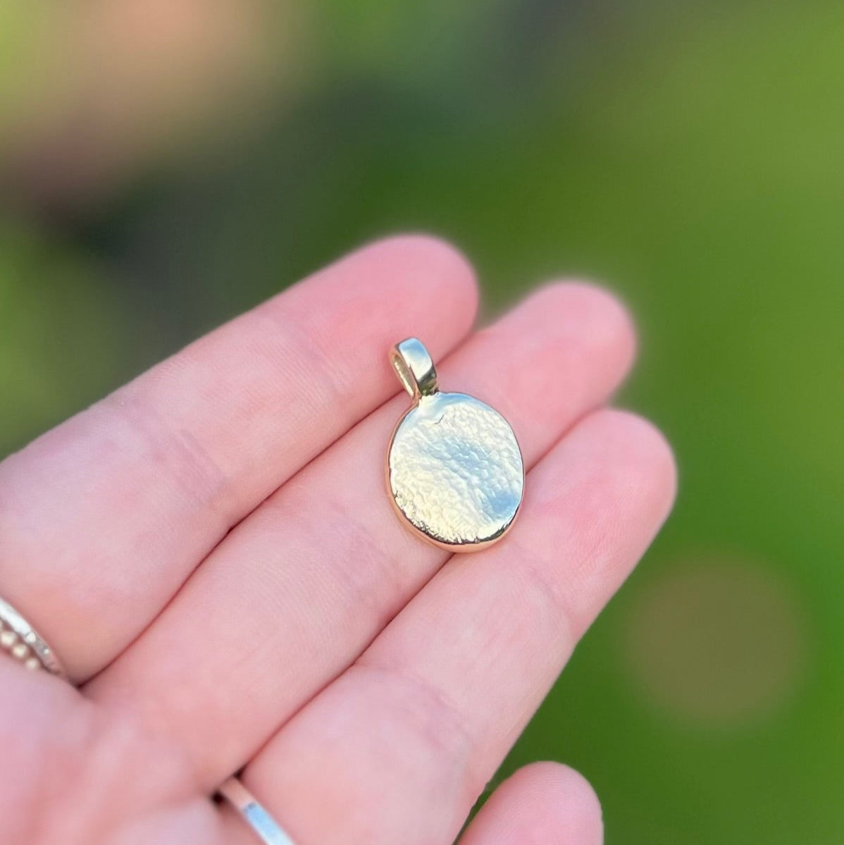 Gold dog nose print pendant held in a hand with a blurred green background