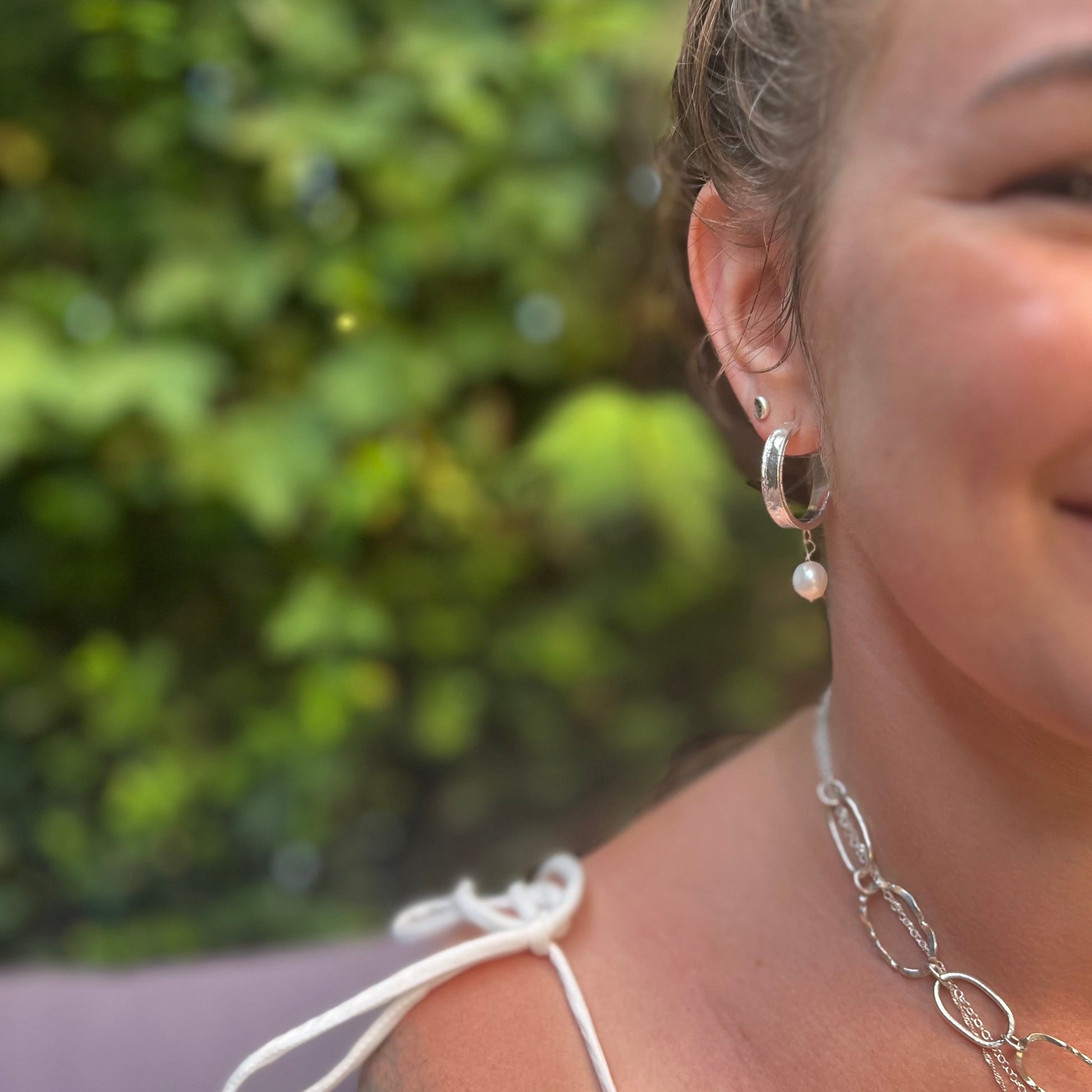 Woman wearing earrings and a necklace with a blurred green background