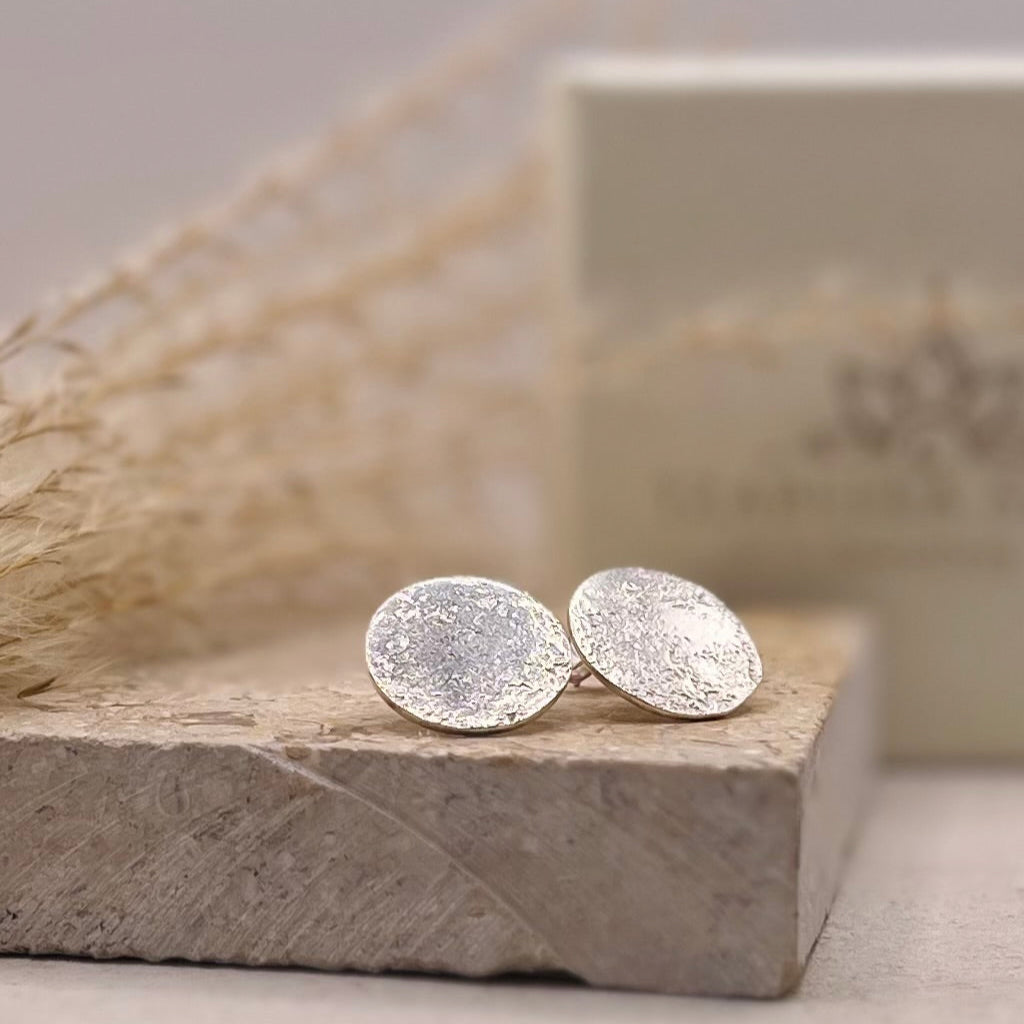 Silver textured earrings on a stone surface with a neutral background