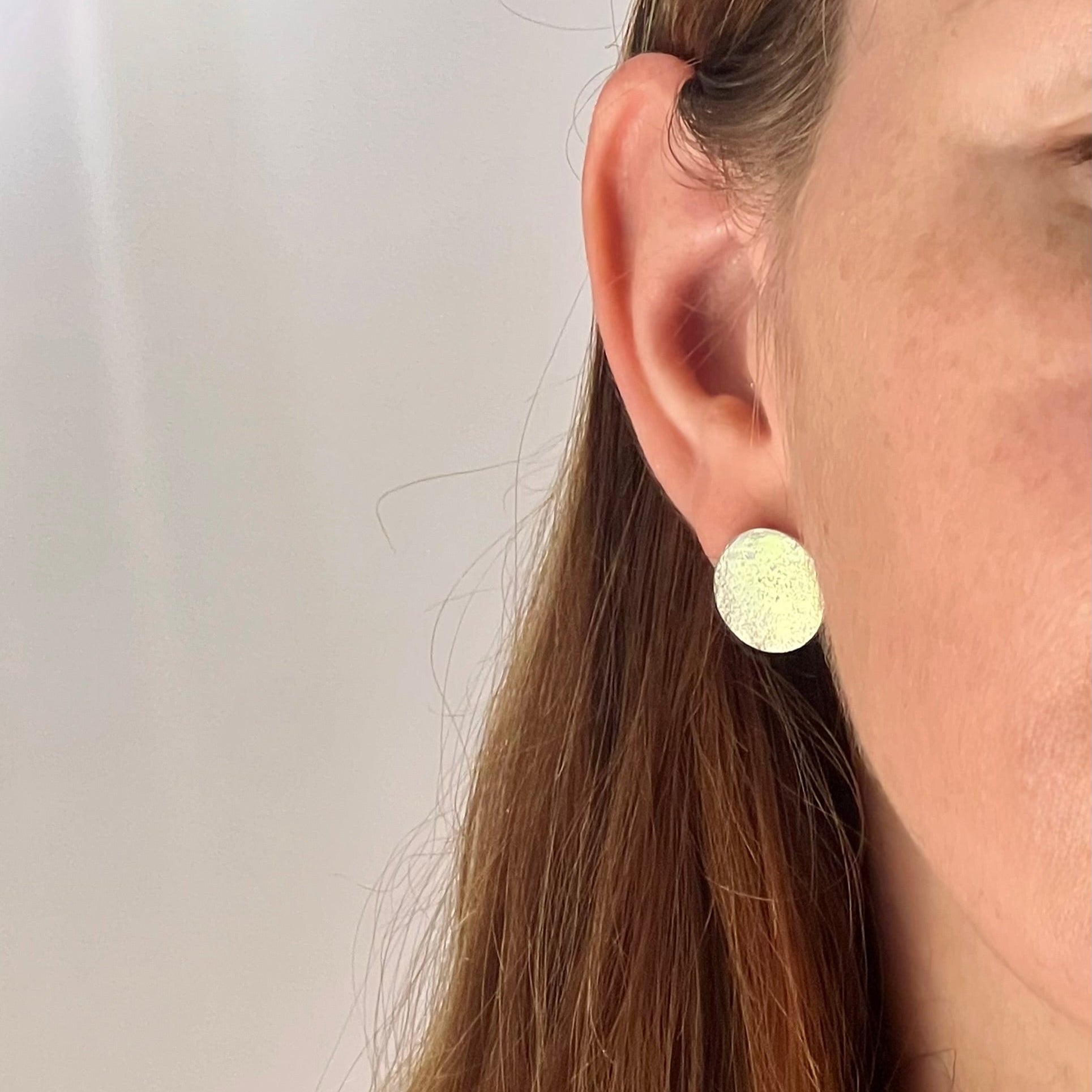 Close-up of a person wearing a silver earring against a plain background
