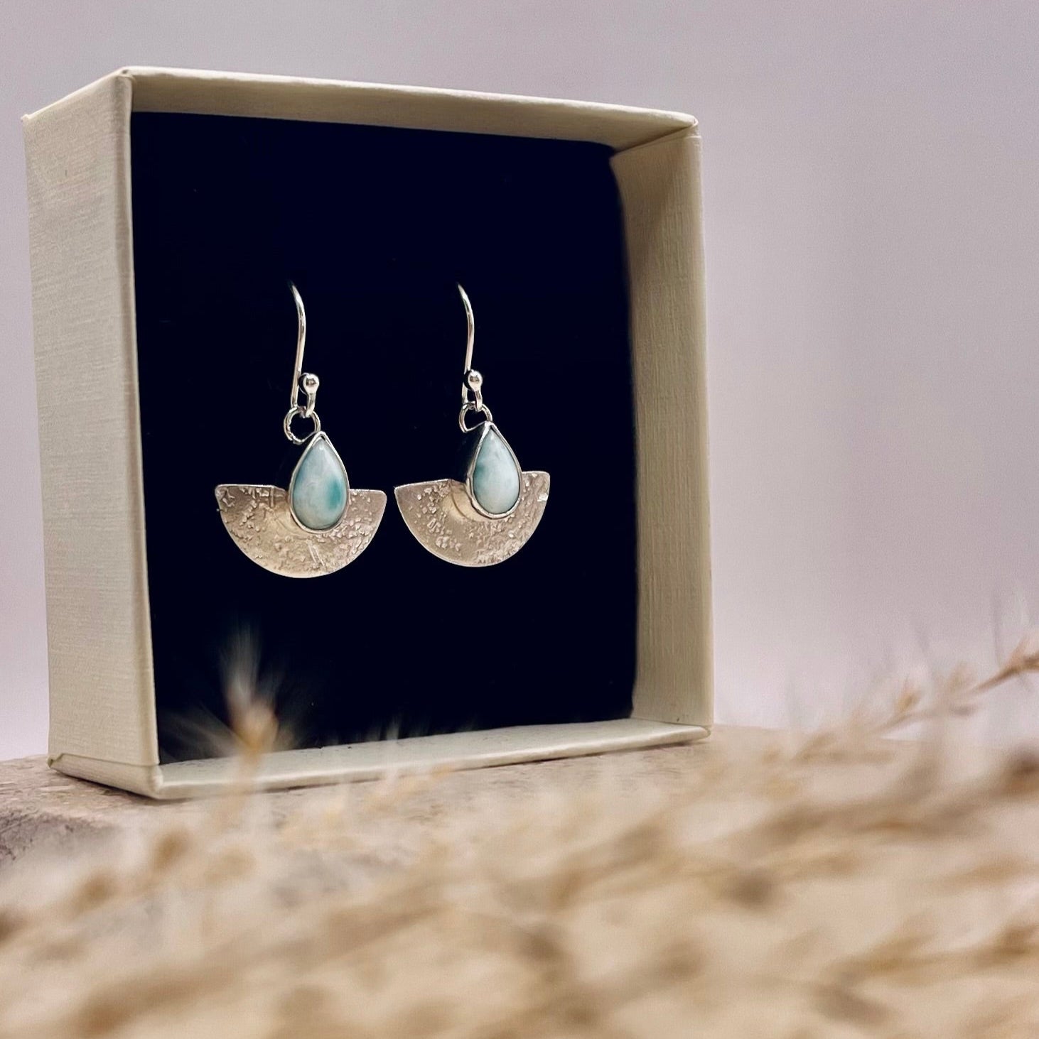 Pair of earrings in a box with a textured surface and light background
