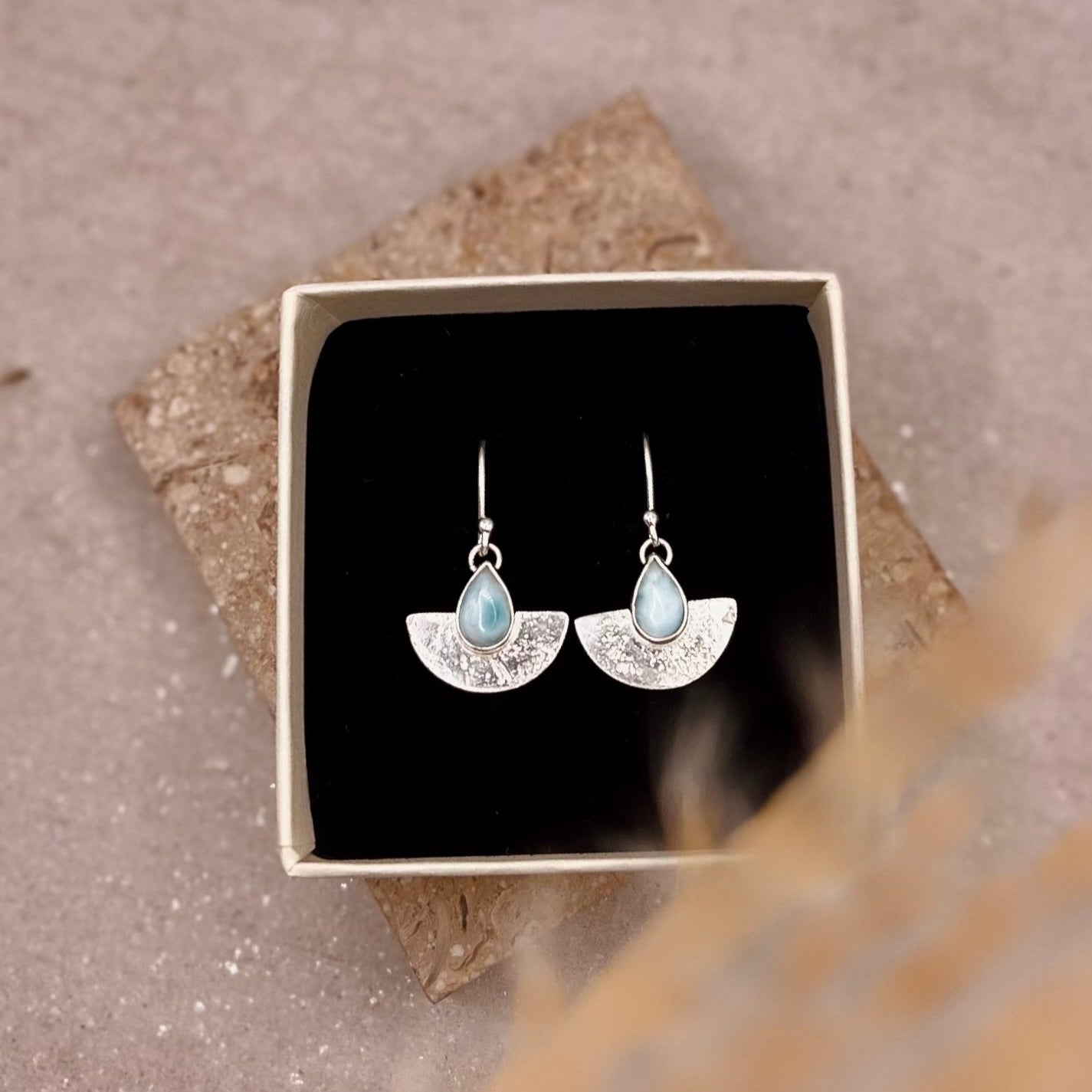 Blue stone Earrings in a box on a textured surface