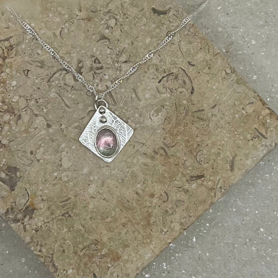 Silver necklace with a pink pendant on a textured stone surface