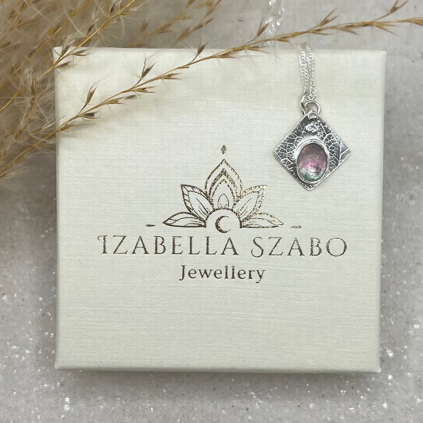 Jewellery pendant on a card with 'Izabella Szabo Jewellery' branding, surrounded by decorative elements.