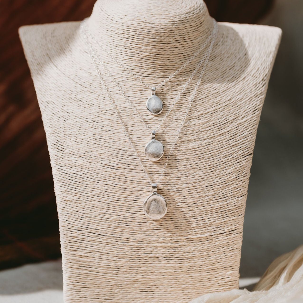 Three different sizes of fingerprint necklaces on a jewellery bust