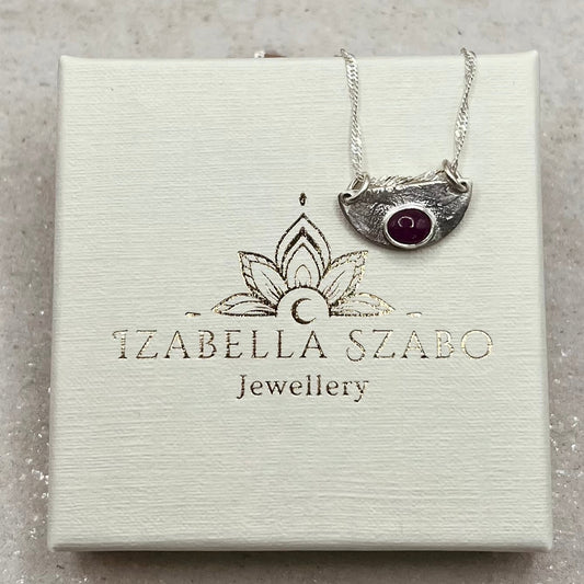 Silver necklace with a red gemstone on a branded jewelry box