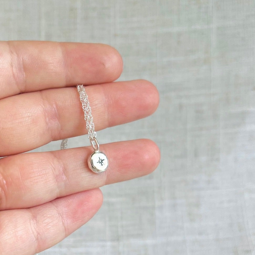 Recycled silver nugget pendant with a star motif, on a silver chain, held in hand. the nugget is about half the size of the width of the finget. 
