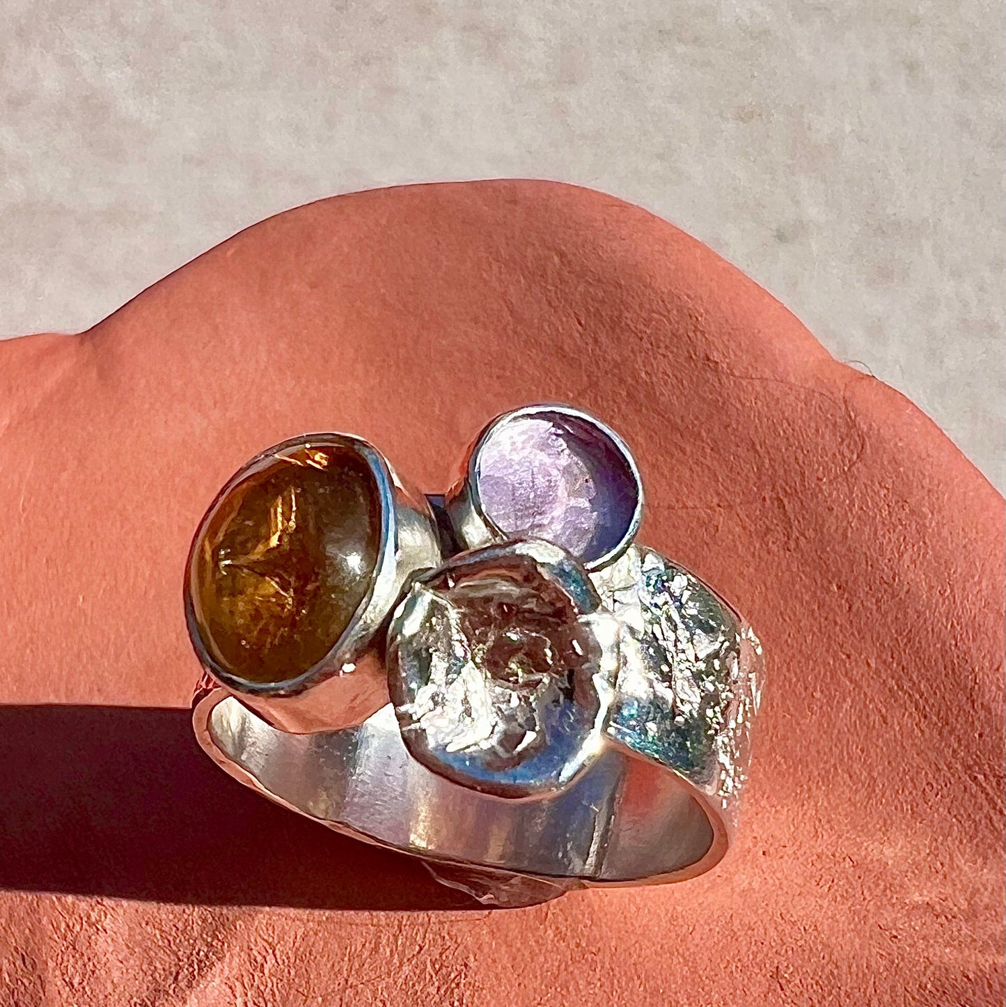 Silver ring with multicolored gemstones on a pink surface