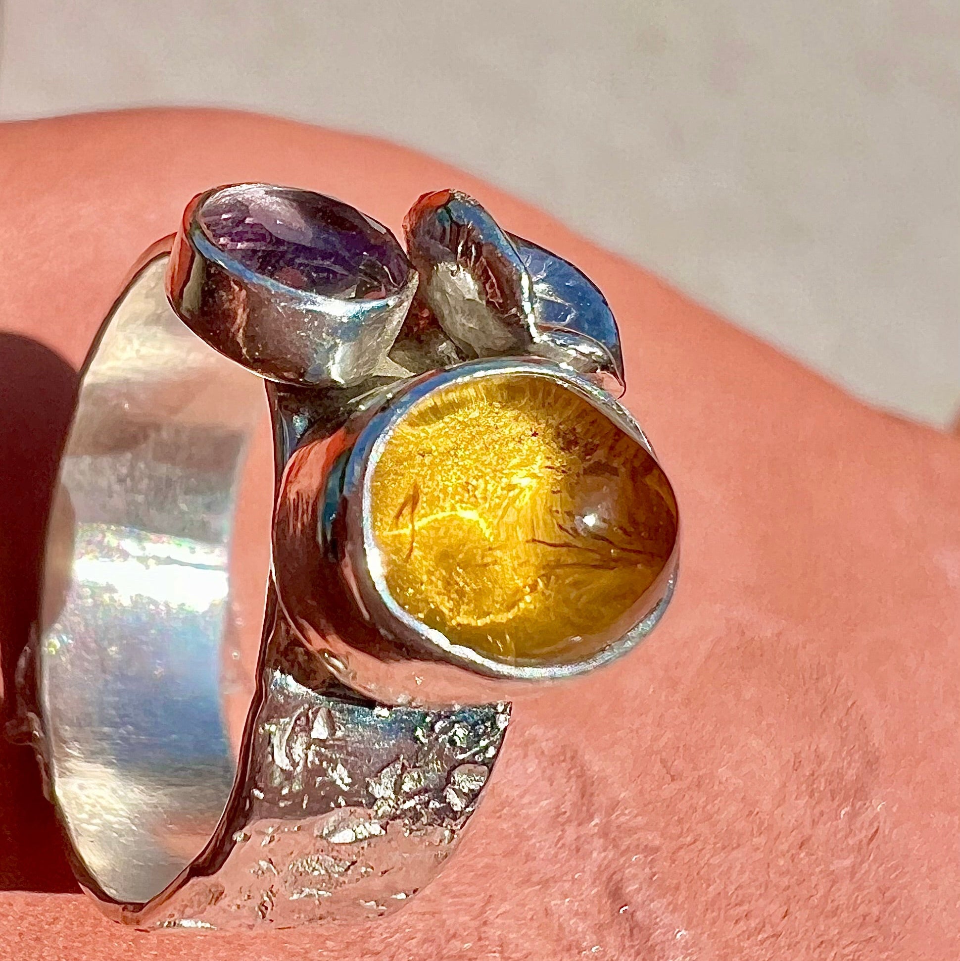 Silver ring with colorful gemstones on a pink surface