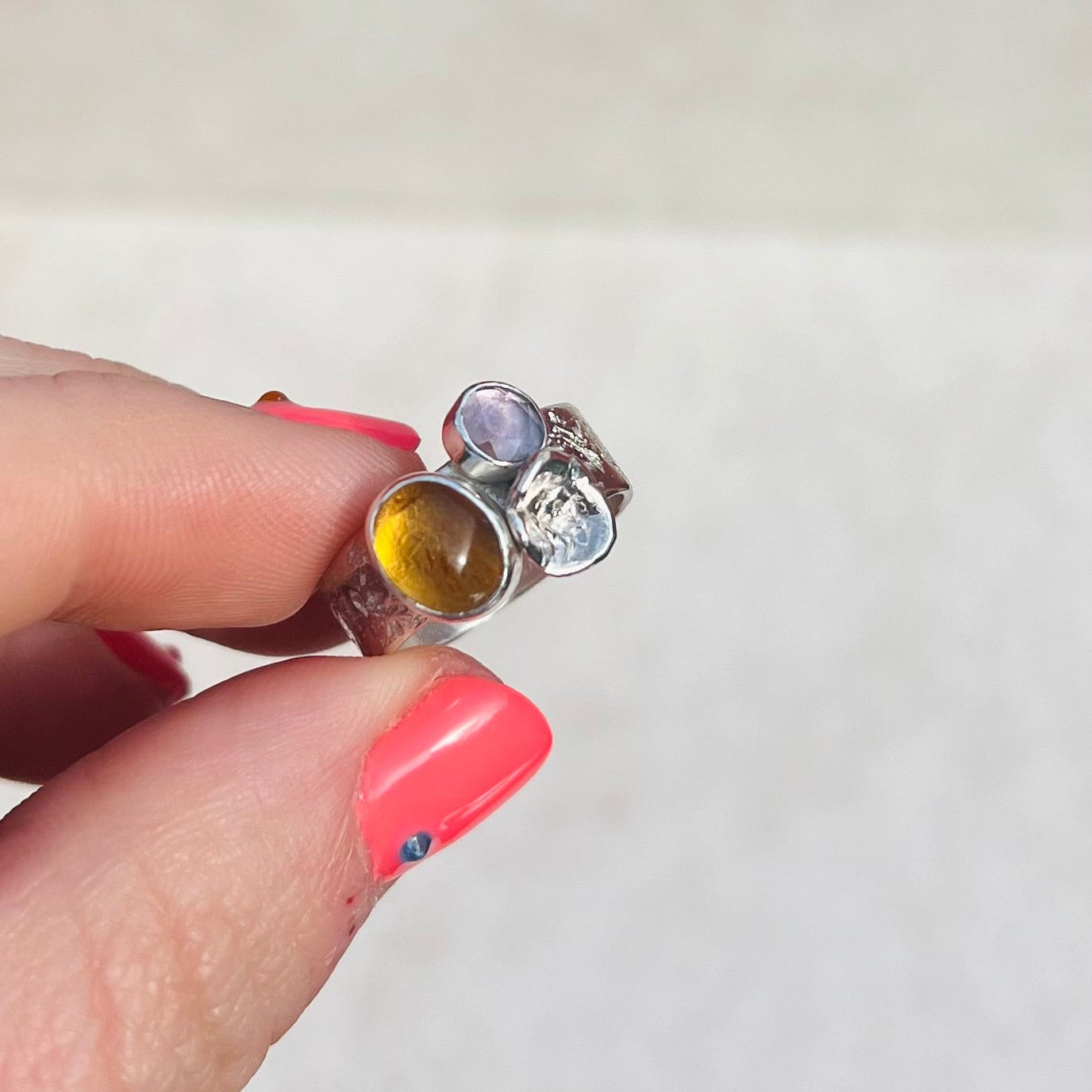 Close-up of a hand holding a silver ring with colored stones against a white background