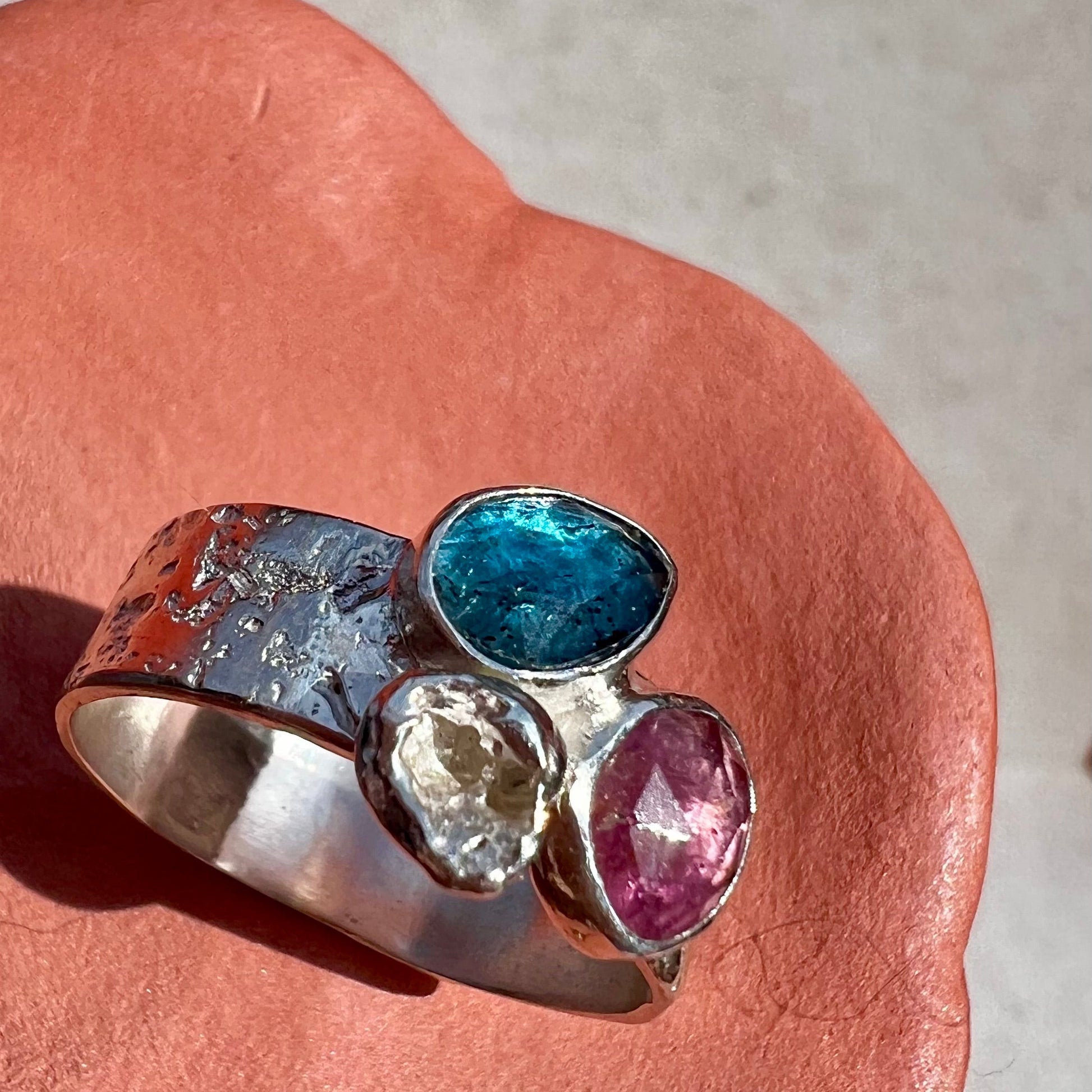 Silver ring with multicolored gemstones on a pink stone surface