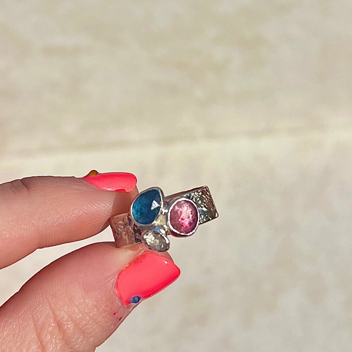 Ring with colorful gemstones held by a hand against a neutral background