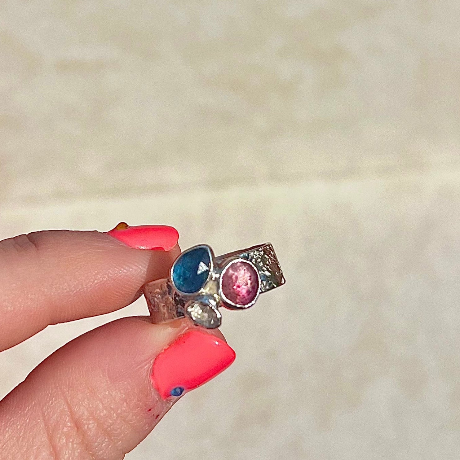 Ring with colorful gemstones held by a hand against a neutral background