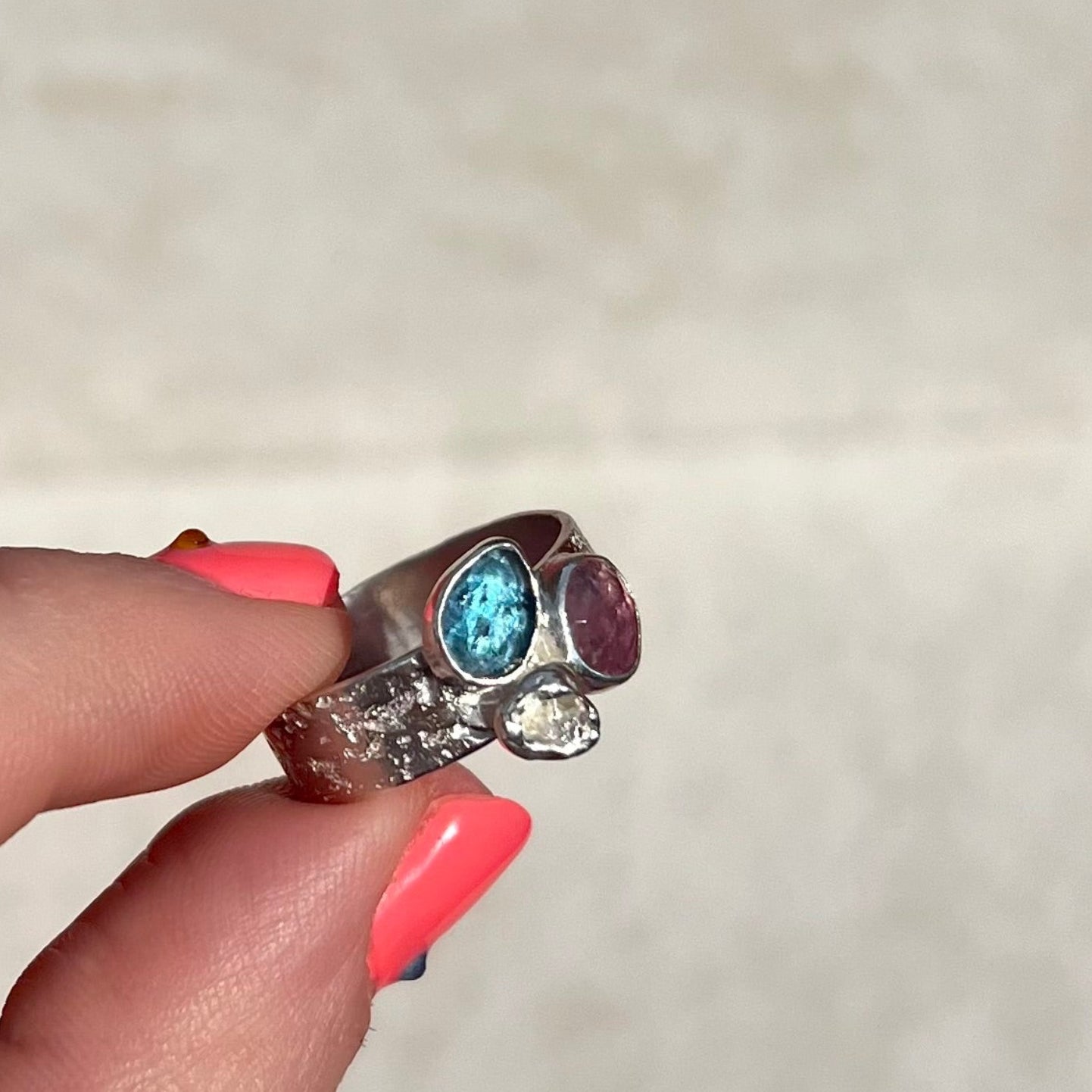 Silver ring with gemstones held by a hand on a neutral background