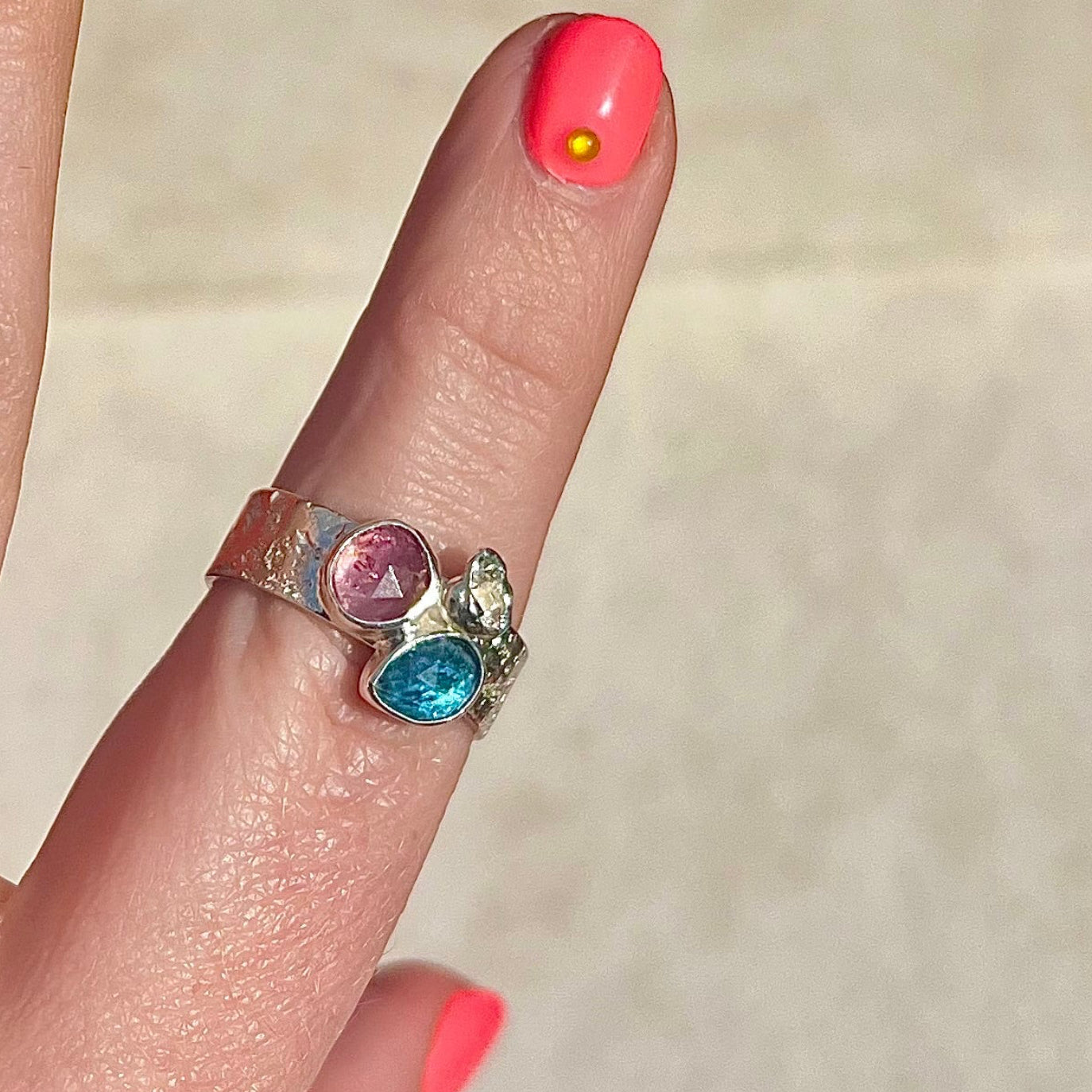 Close-up of a hand wearing a ring with colorful gemstones on a neutral background