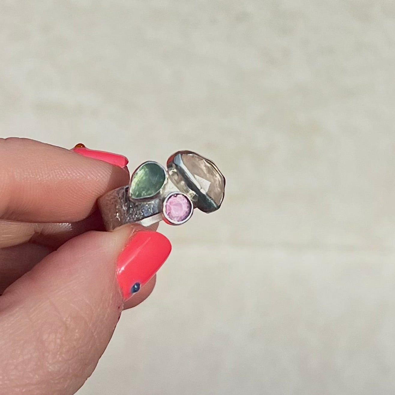 Silver ring with gemstones held by a hand against a neutral background