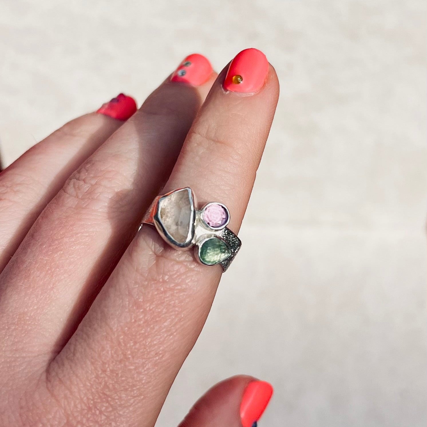 Hand wearing a ring with colorful stones on a neutral background