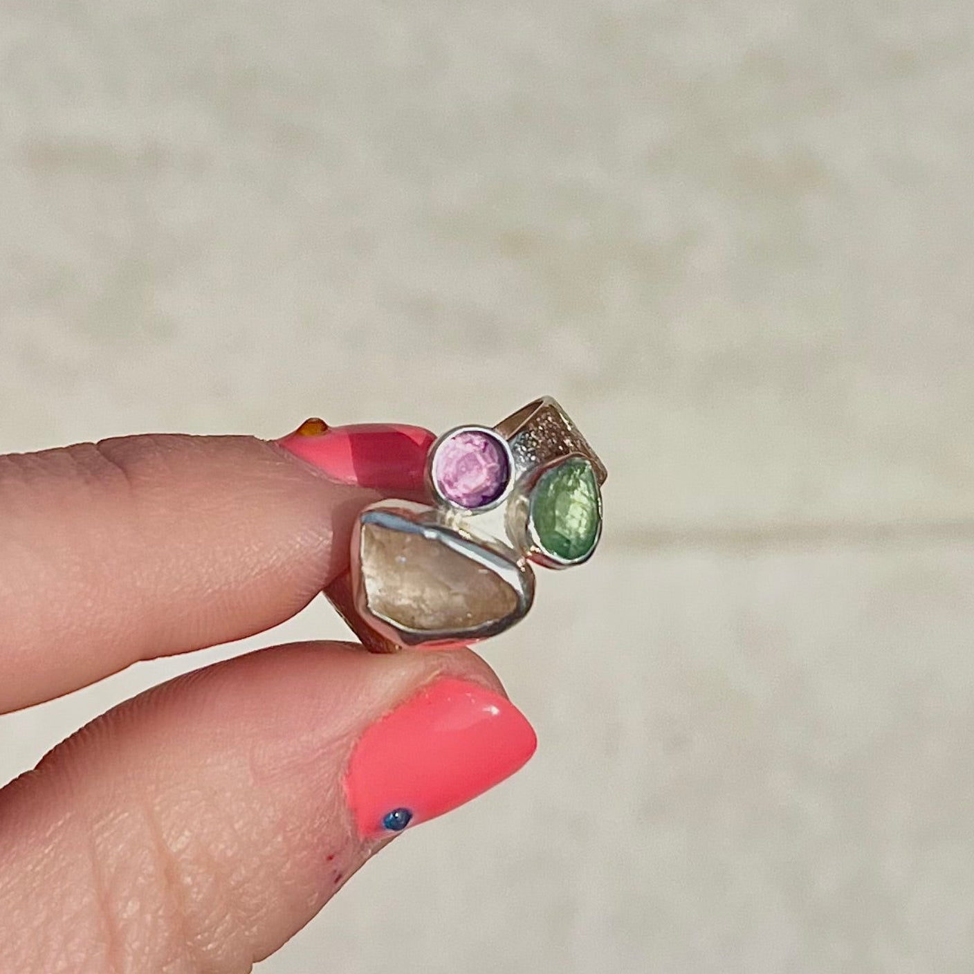 Silver ring with multicolored gemstones held by a hand against a neutral background