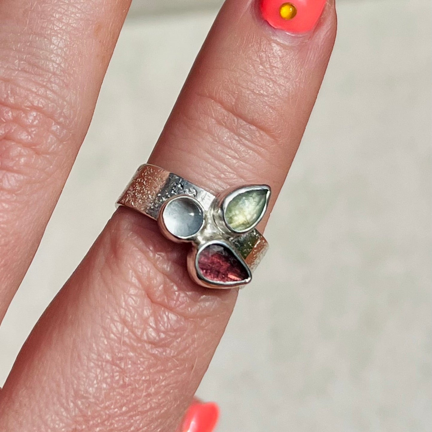Close-up of a hand wearing a silver ring with gemstones on a neutral background