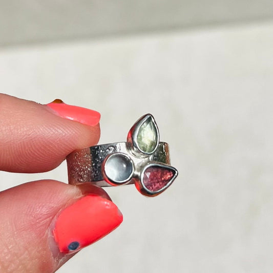 Silver ring with gemstones held by a hand with pink nail polish on a white background