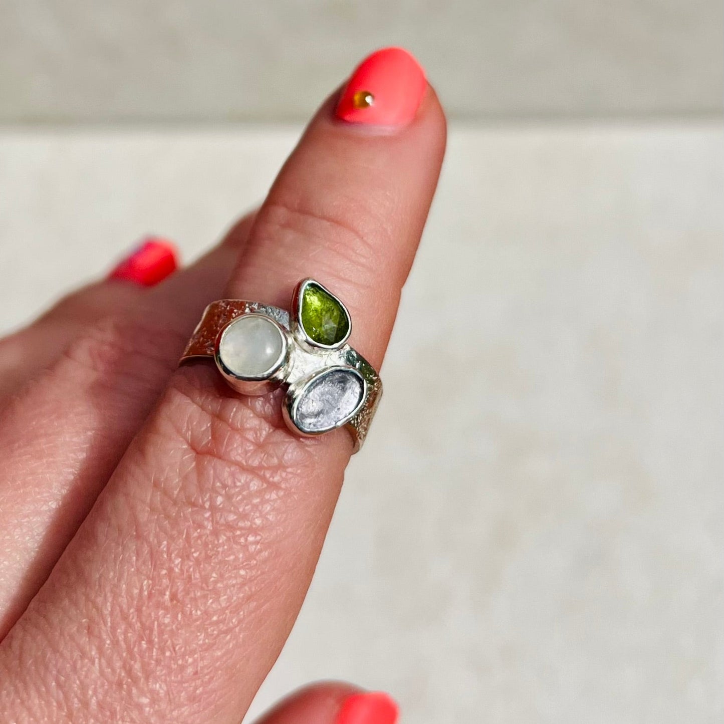 Close-up of a hand wearing a ring with three gemstones on a neutral background