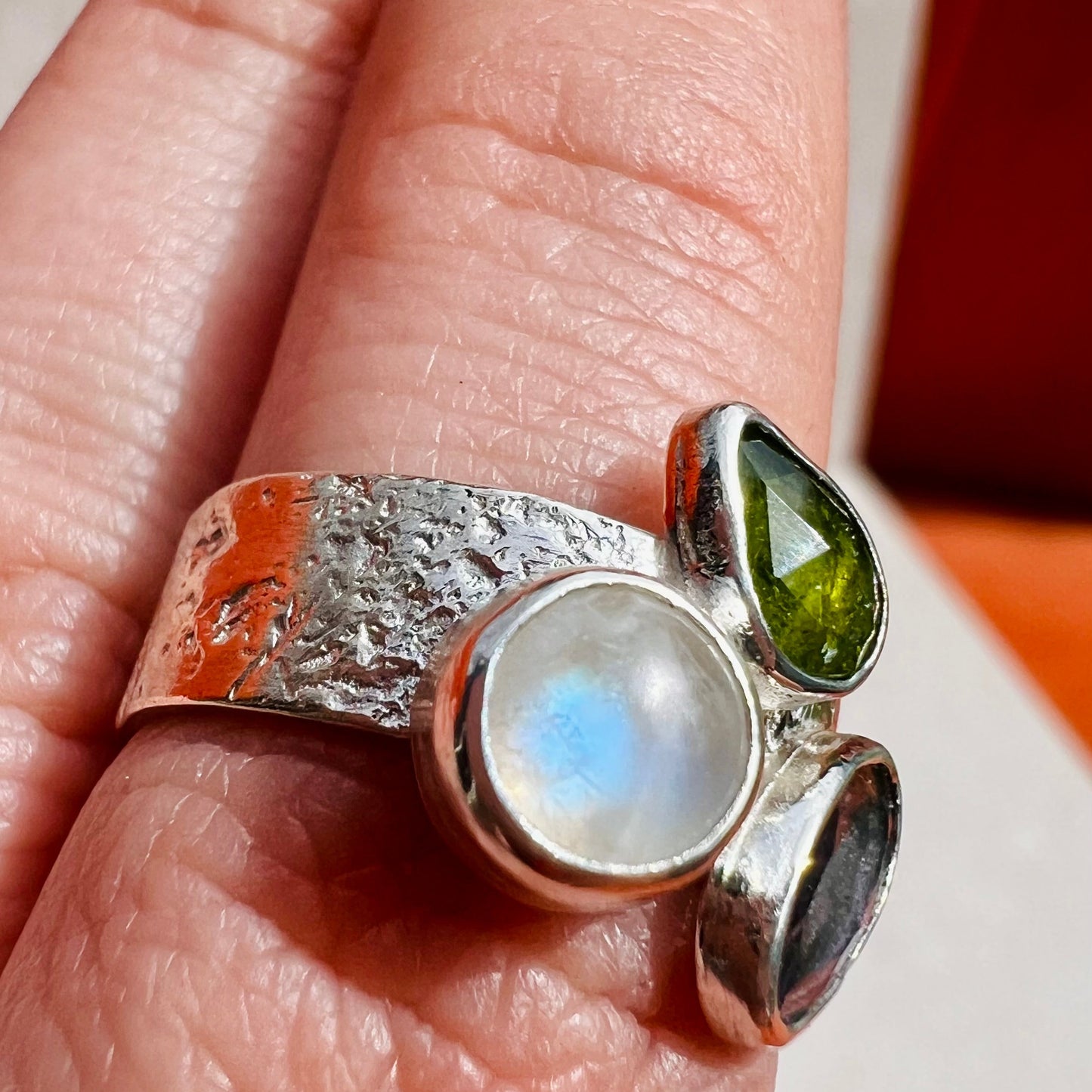 Silver ring with moonstone and green stone on a finger