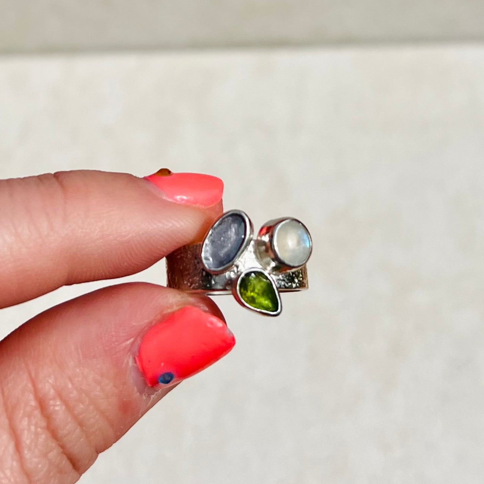 Close-up of a hand holding a pair of silver earrings with gemstones against a neutral background
