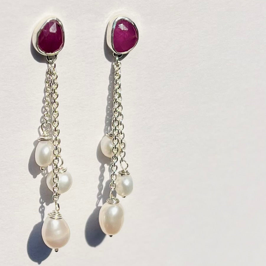 Pair of earrings with purple gemstones and pearl drops on a light gray background