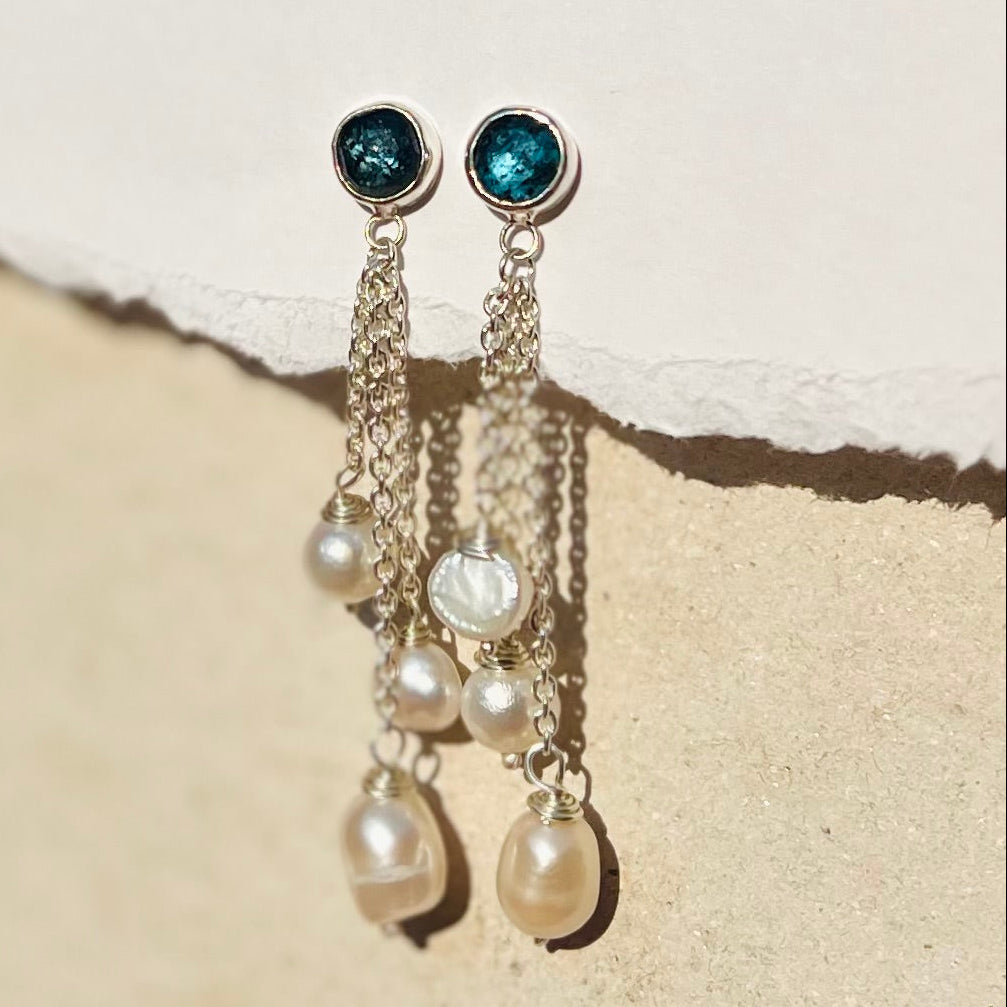 Pair of earrings with blue gemstones and pearl drops on a textured beige surface