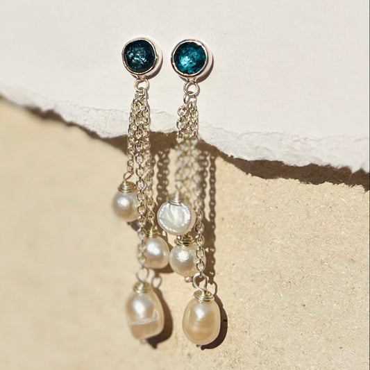 Pair of earrings with blue gemstones and pearl drops on a textured beige surface