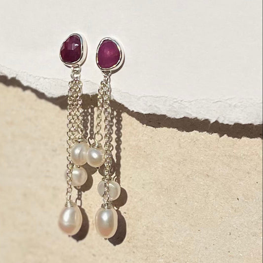 Earrings with red gemstones and pearl drops on a textured surface