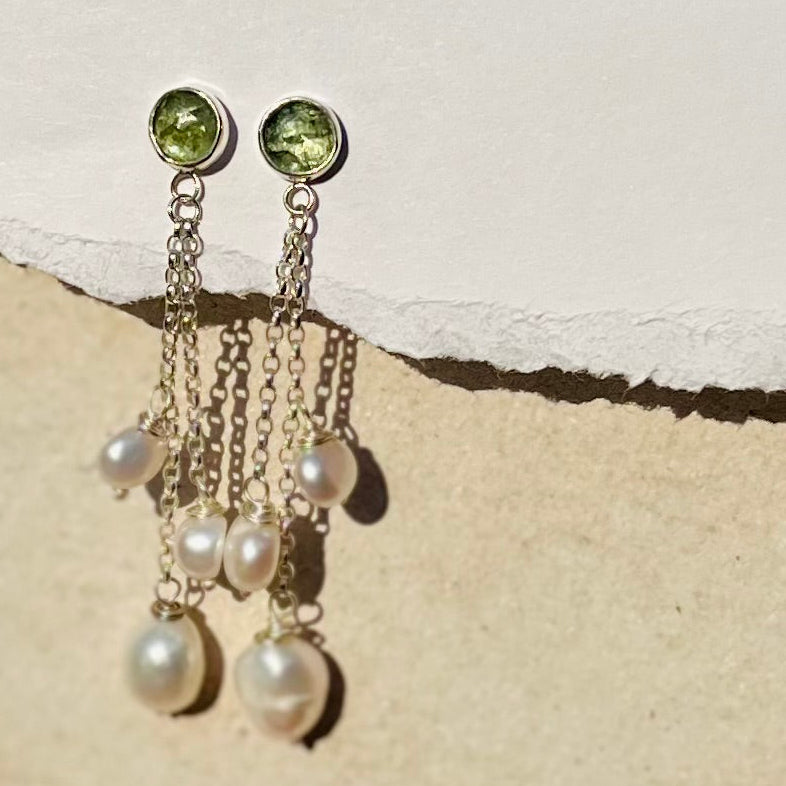 Pair of earrings with green gemstones and pearl-like beads on a textured beige surface