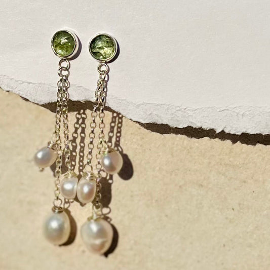 Pair of earrings with green gemstones and pearl-like beads on a textured beige surface
