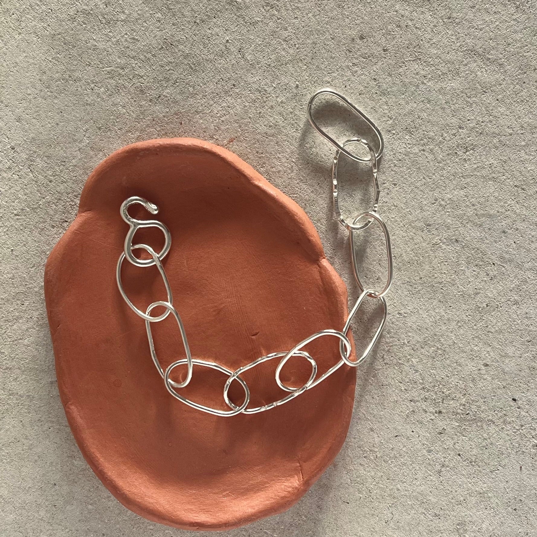 Silver chain on a brown ceramic dish against a gray background