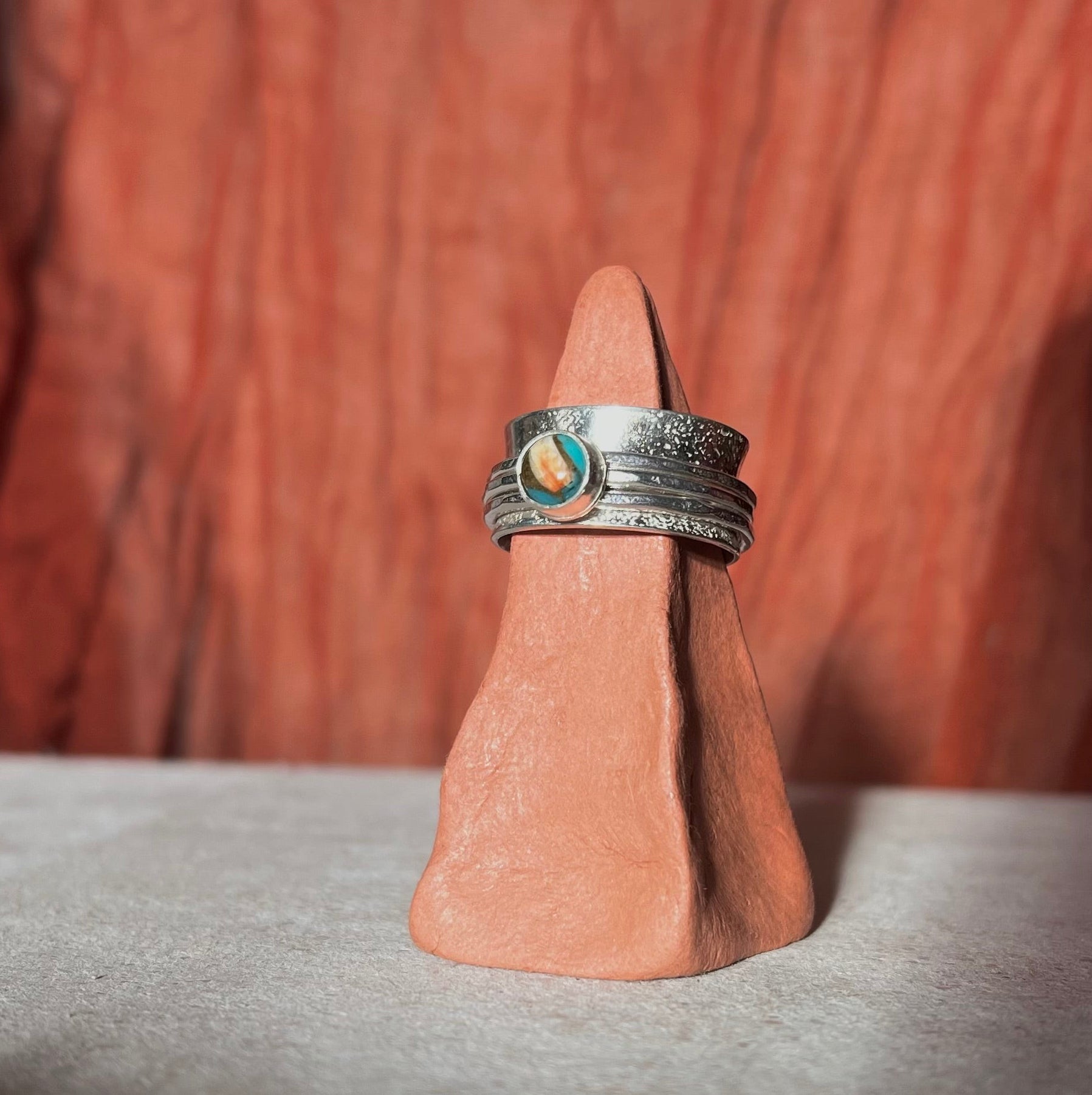 Silver ring with a green stone on a wooden stand against a brown background