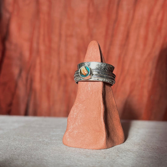Silver ring with a green stone on a wooden stand against a brown background