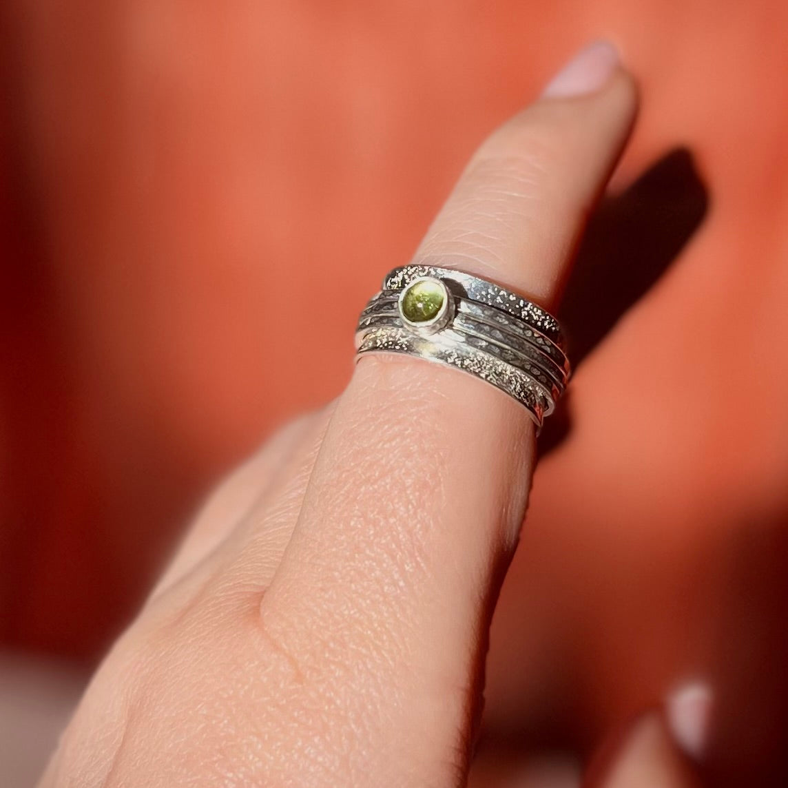 Silver ring with a green gemstone on a finger against a blurred background