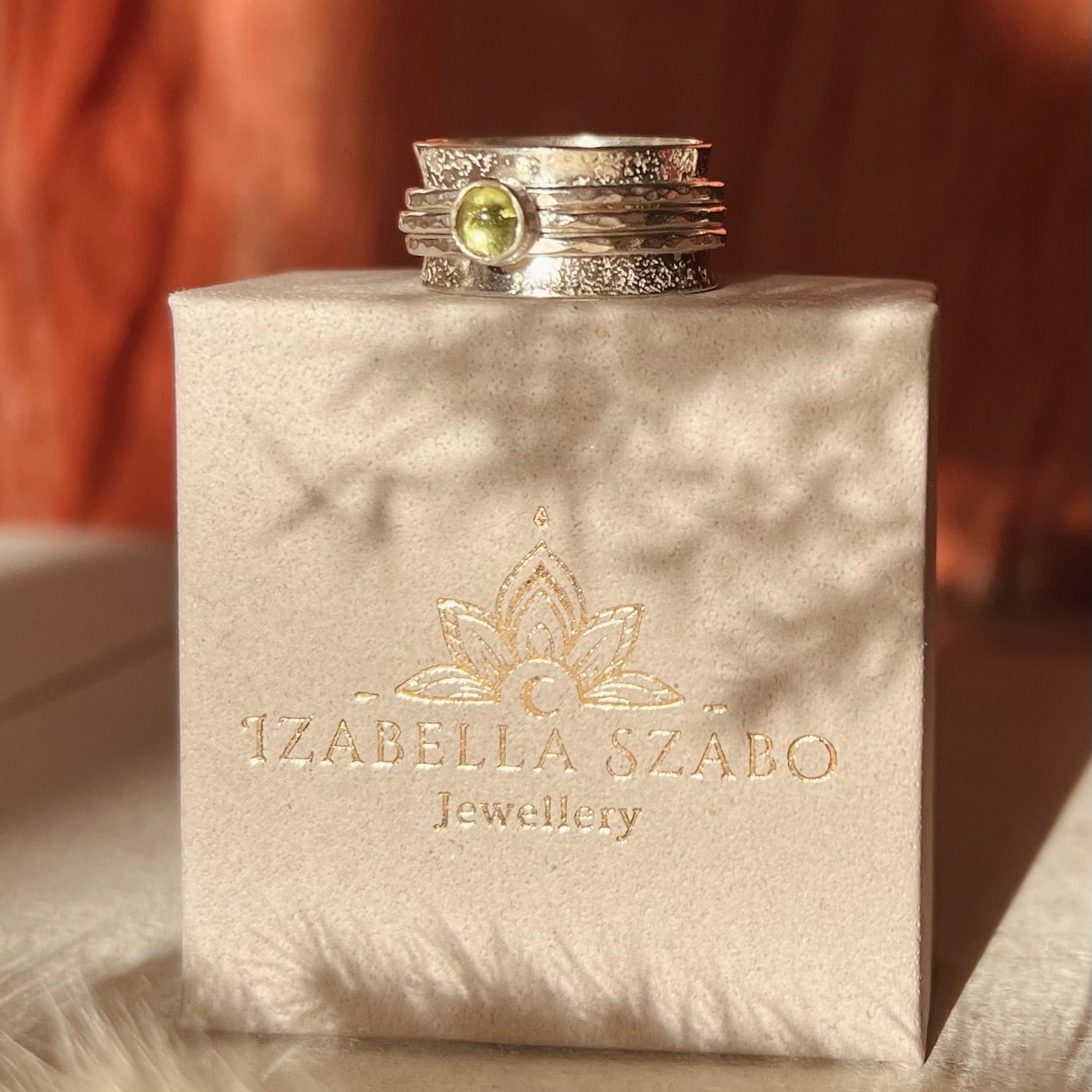 Stack of silver rings with a green gemstone on an Izabella Szabo jewelry box.