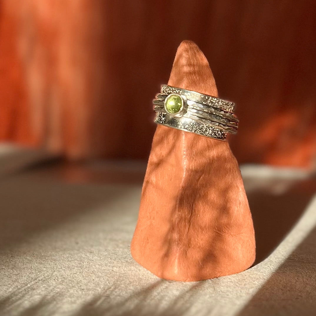 Silver ring with a green gemstone on a wooden block against a blurred background