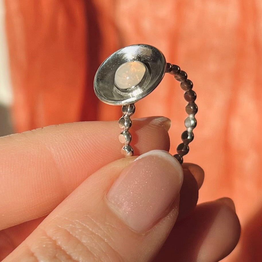 Silver ring with a small round object held between fingers against an orange background